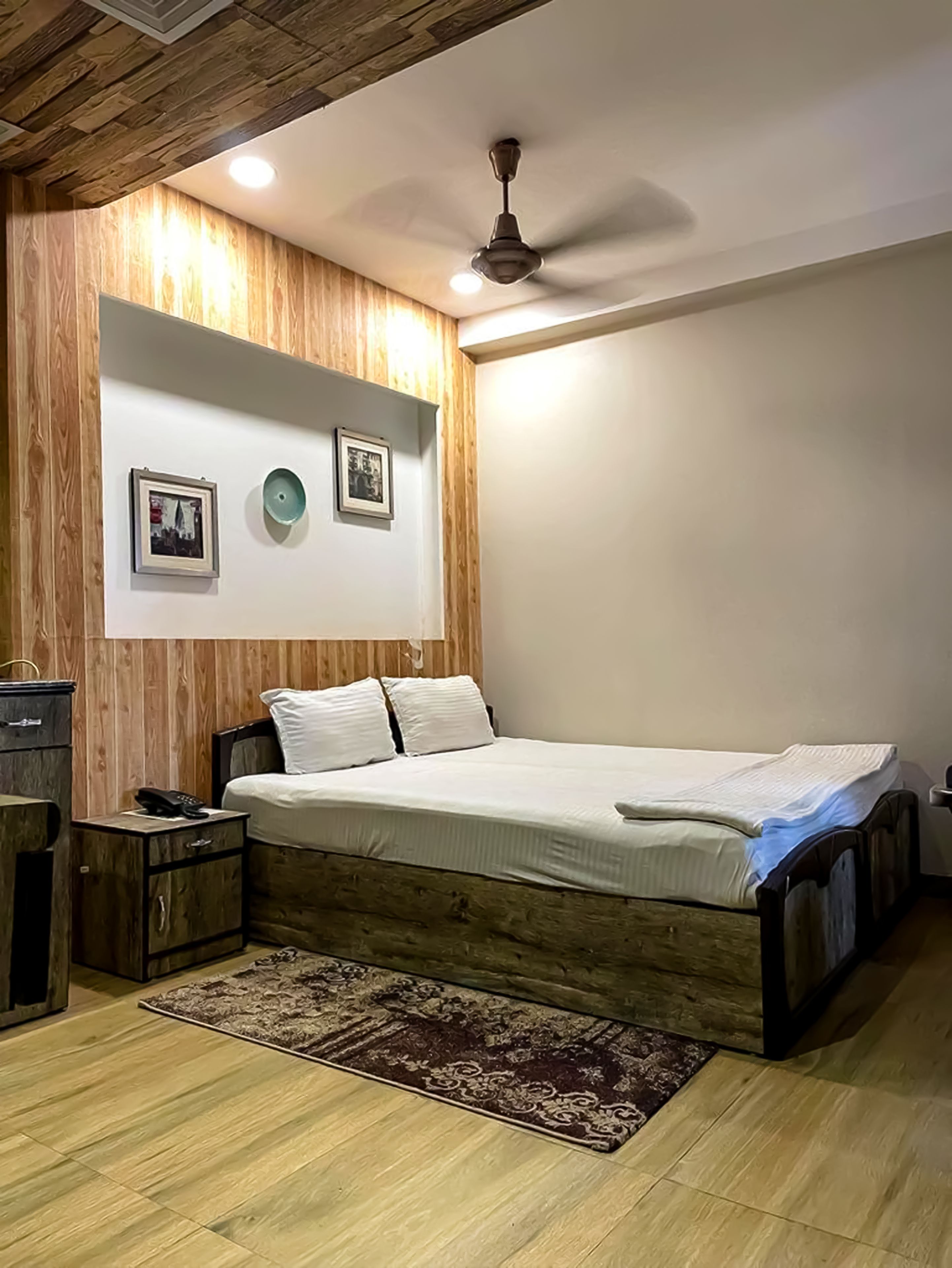 Un dormitorio con estructura de cama de madera, mesita de noche, teléfono y lámpara fijada a la pared.