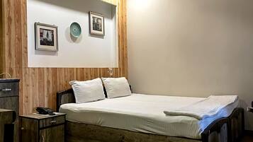 Un dormitorio con estructura de cama de madera, mesita de noche, teléfono y lámpara fijada a la pared.