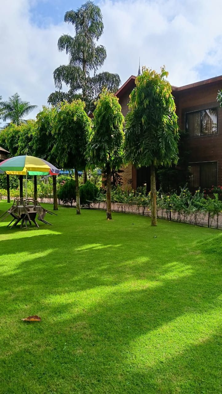 Zona verde y cuidada con una mesa de picnic y sombrilla, rodeada de árboles y un edificio de fachada de ladrillo.