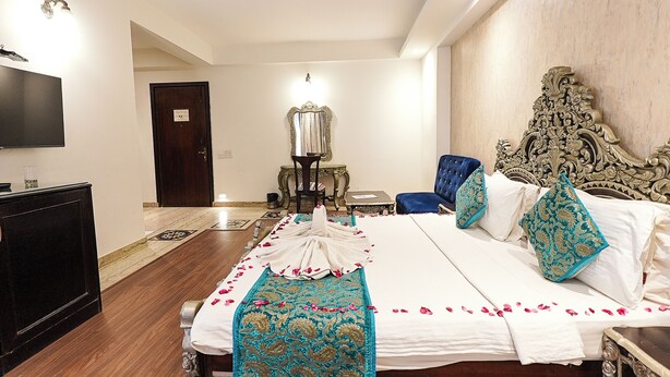 A hotel room with a large bed, a flat-screen TV, a desk, and a chair. - Hotel Maple Ridge  (Agra)