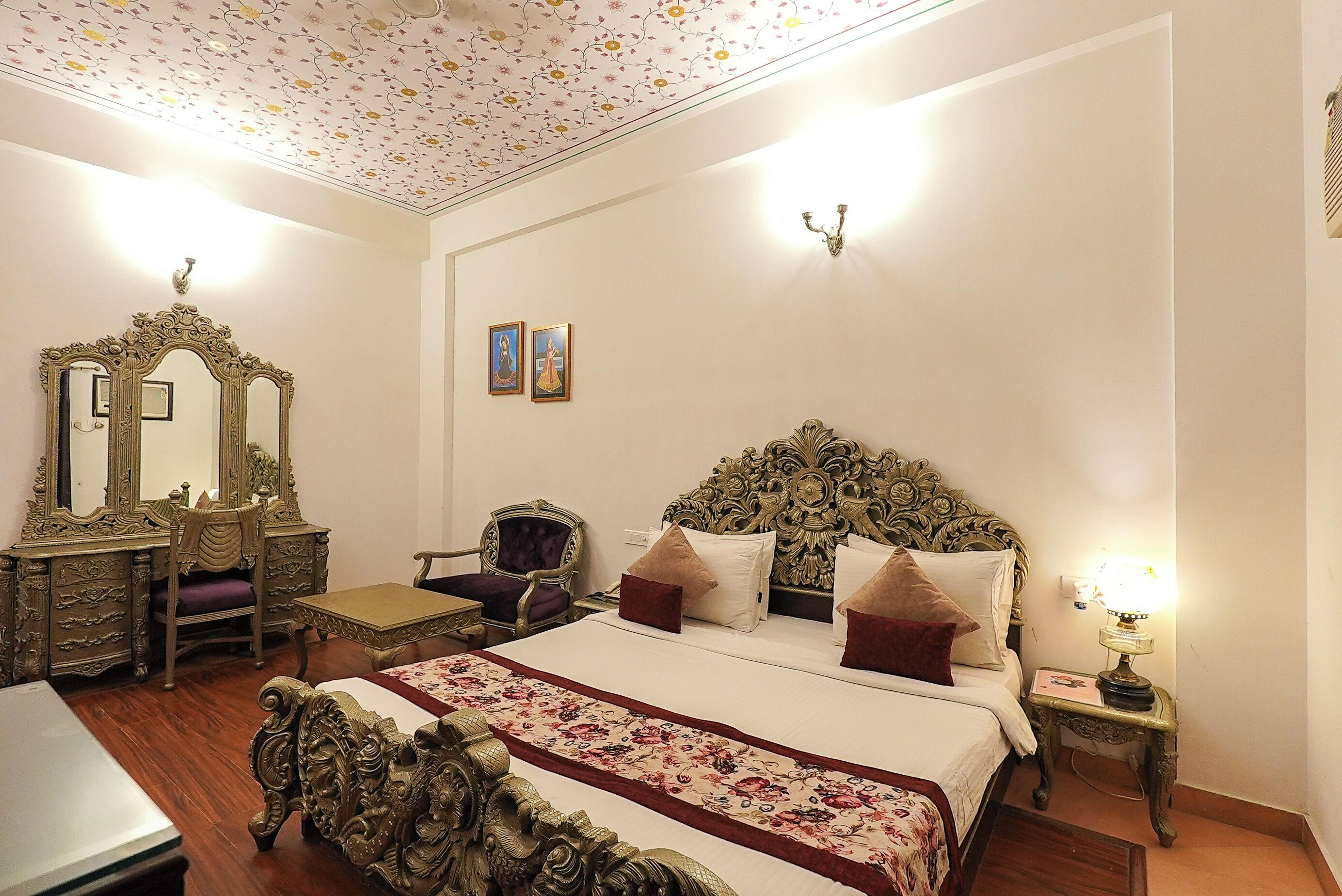 A bedroom with a large ornate bed, a vanity with a mirror, a desk, and a chair.