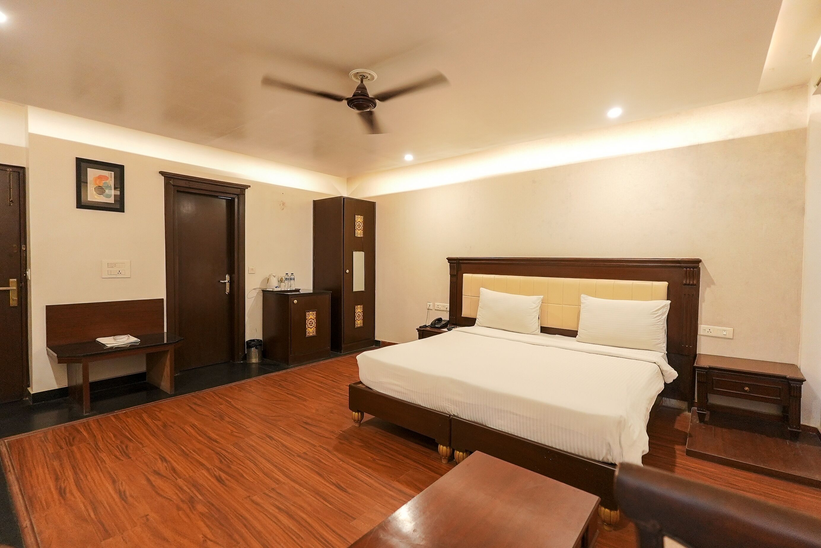 A hotel room with a large bed, a desk, a chair, a wardrobe, and a ceiling fan.