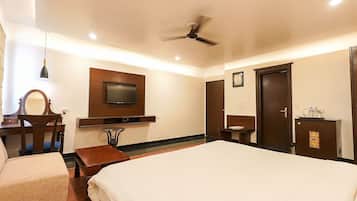Habitación de hotel con cama, escritorio con silla, televisor montado en la pared, ventilador de techo y armario.