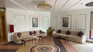 A lobby with sofas, a central rug, and artwork on the walls. - Hotel Maple Ridge  (Agra)