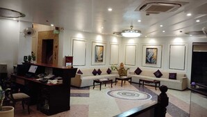 A hotel lobby with a reception desk, seating area, and artwork on the walls. - Hotel Maple Ridge  (Agra)