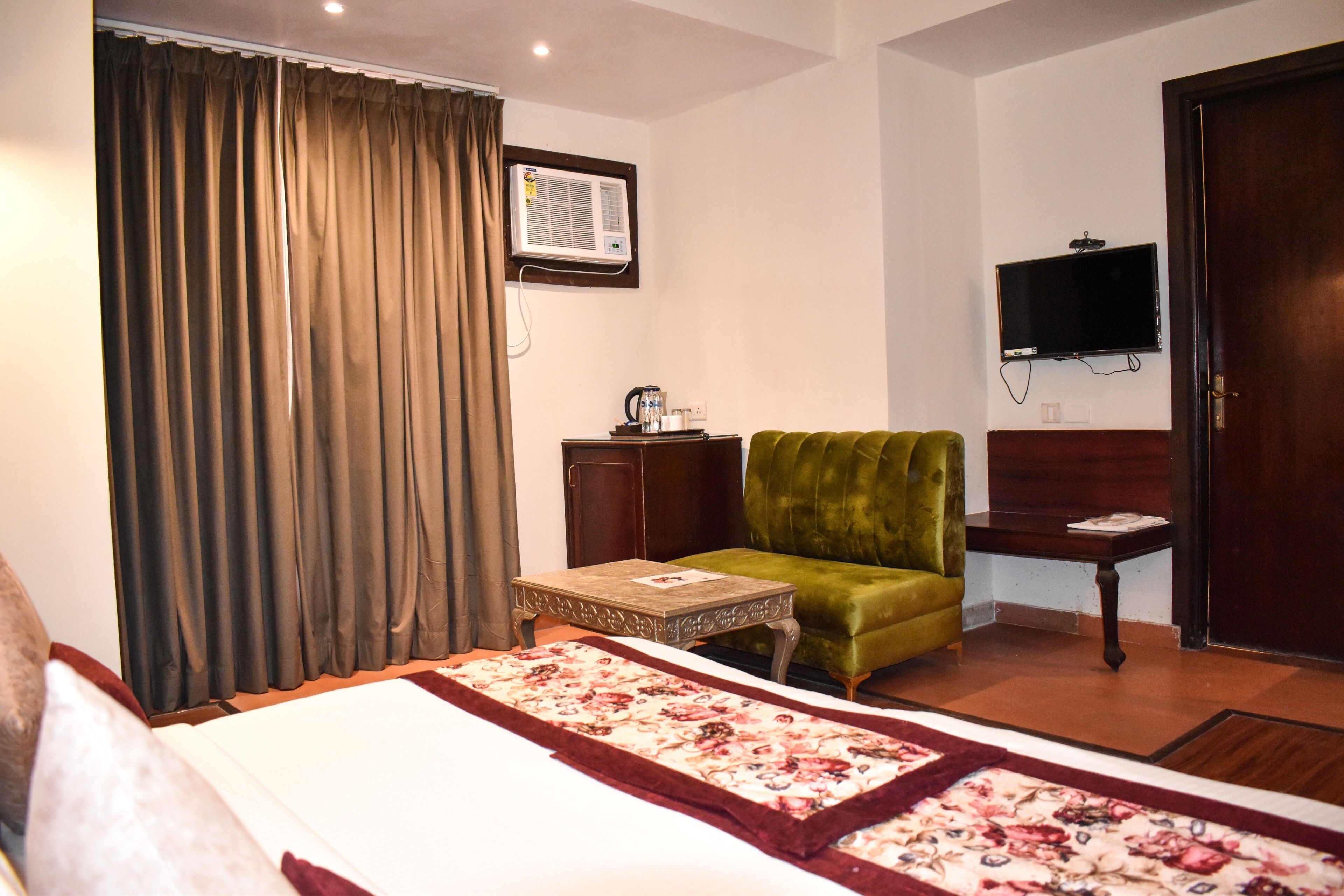 Une chambre d’hôtel avec un lit, un fauteuil vert, une petite table, un téléviseur et un appareil de climatisation.