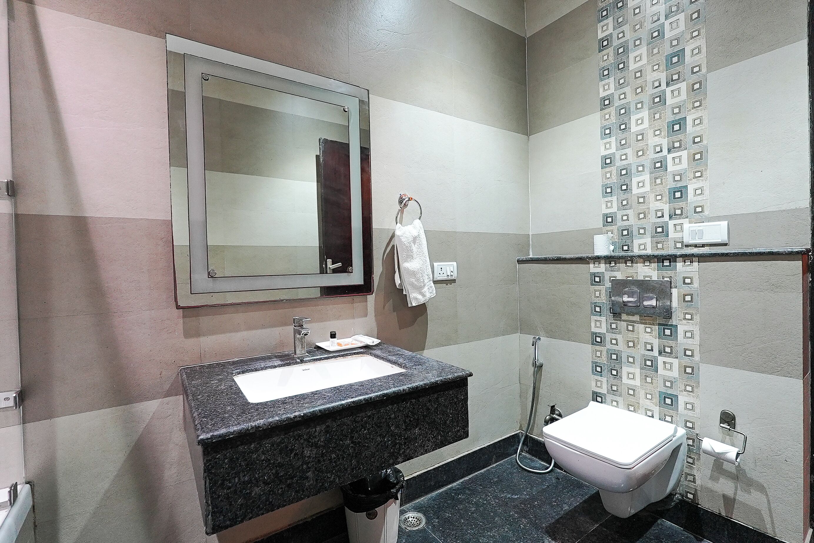 Un baño con lavamanos de granito, espejo, inodoro y ducha.