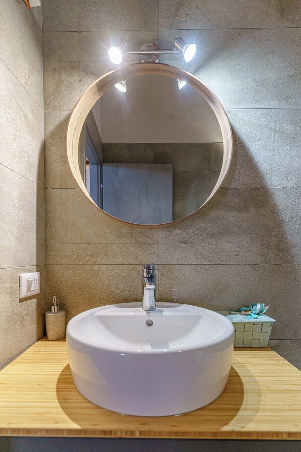 A bathroom with a round mirror, a white sink, and a wooden vanity. - Le dimore del mito - Gaia (Syracuse)