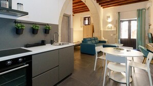 Eine moderne Küche mit Einbauherd, Spüle und Topfpflanzen. Ein Essbereich mit weißem Tisch und Stühlen, im Hintergrund ein blaues Sofa.