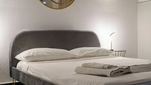 Ein modernes Schlafzimmer mit grauem gepolsterten Kopfteil, weißer Bettwäsche und einem Nachttisch mit Lampe.