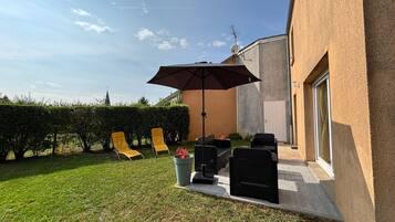 Une terrasse avec des meubles d’extérieur, un grand parasol et une haie.