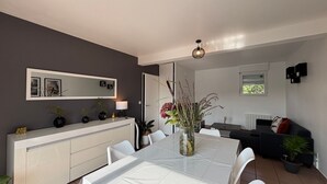 A modern dining area with a white table and chairs, a white console table with decorative items, a dark grey wall, and a window with blinds.