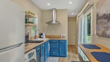 A modern kitchen with blue cabinets, a stainless steel range hood, and a large window providing natural light.