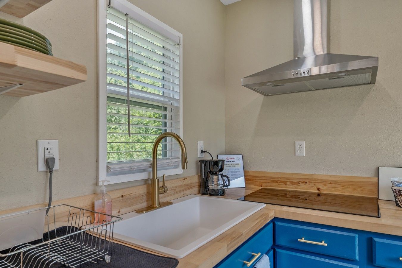 Una cocina moderna con campana de acero inoxidable, una ventana con persianas, cafetera y armarios azules.