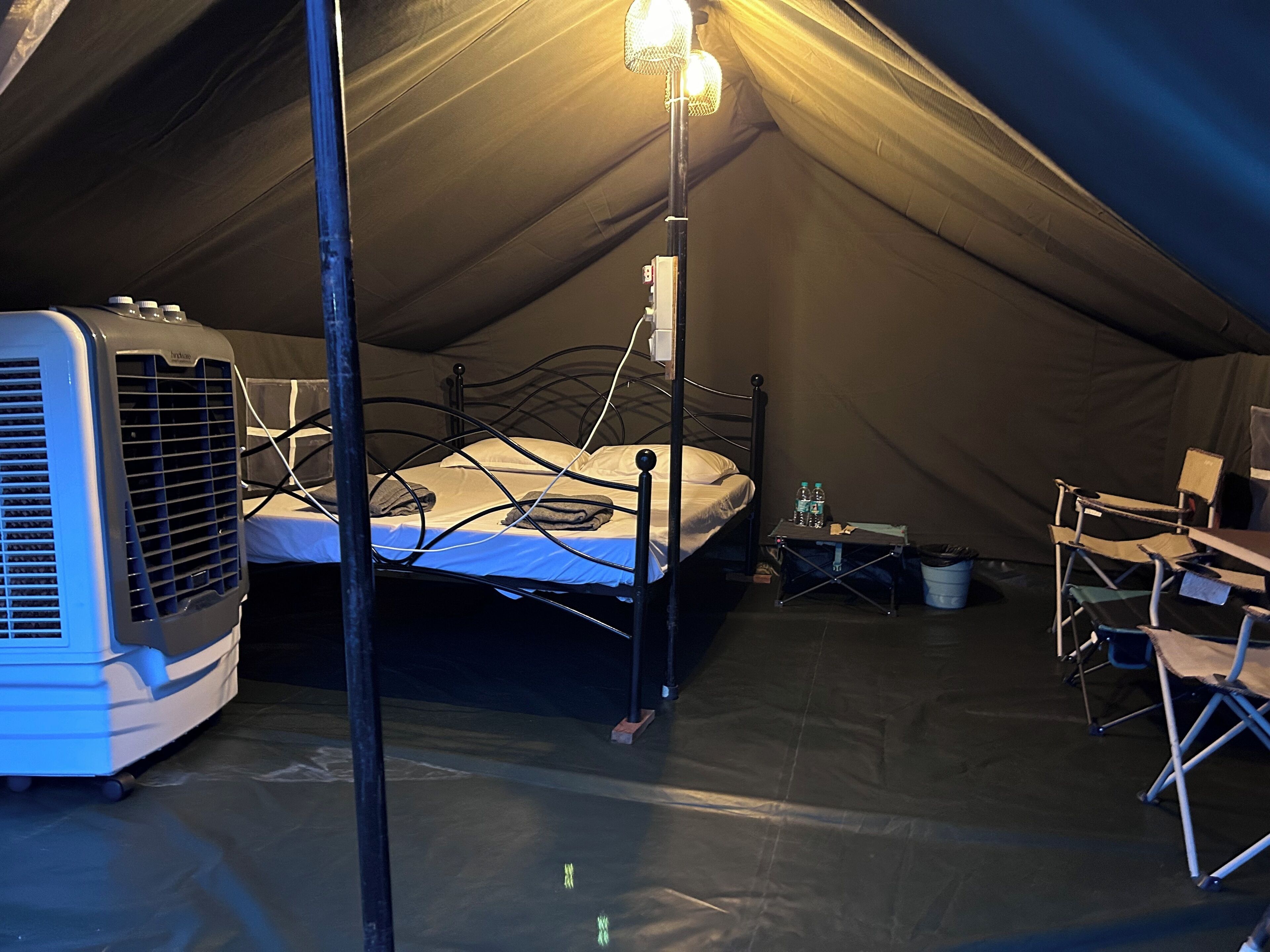A tented room with a bed, a heater, and a table with chairs.