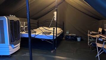 A tented room with a bed, a heater, and a table with chairs.