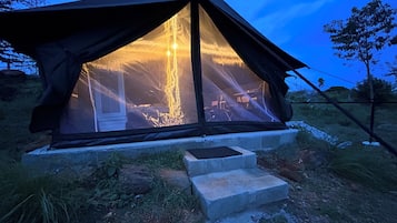 A tent with a large window, set on a grassy area with steps leading up to it.