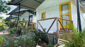 Een landelijk gebouw met een witte gevel en gele accenten, omgeven door weelderig groen en een overdekt terras.