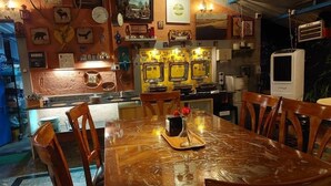 Een restaurant met een houten tafel en stoelen, een keuken met apparatuur en diverse wanddecoraties.