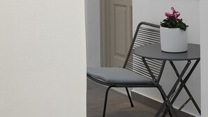 A small outdoor seating area with a table and a chair, a potted plant, and a door with a light above it.