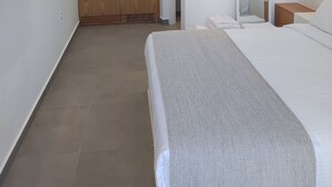 A modern hotel room with a large bed, a flat-screen TV mounted on the wall, a small kitchen area with a sink and cabinets, and a mirror.