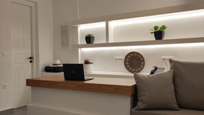 A modern, minimalist living space with a wooden console table, a laptop, and a sofa with cushions. There are two potted plants on a shelf above the table.