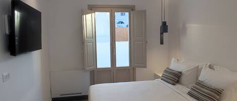 A modern bedroom with a bed, a TV mounted on the wall, and a window with open shutters.
