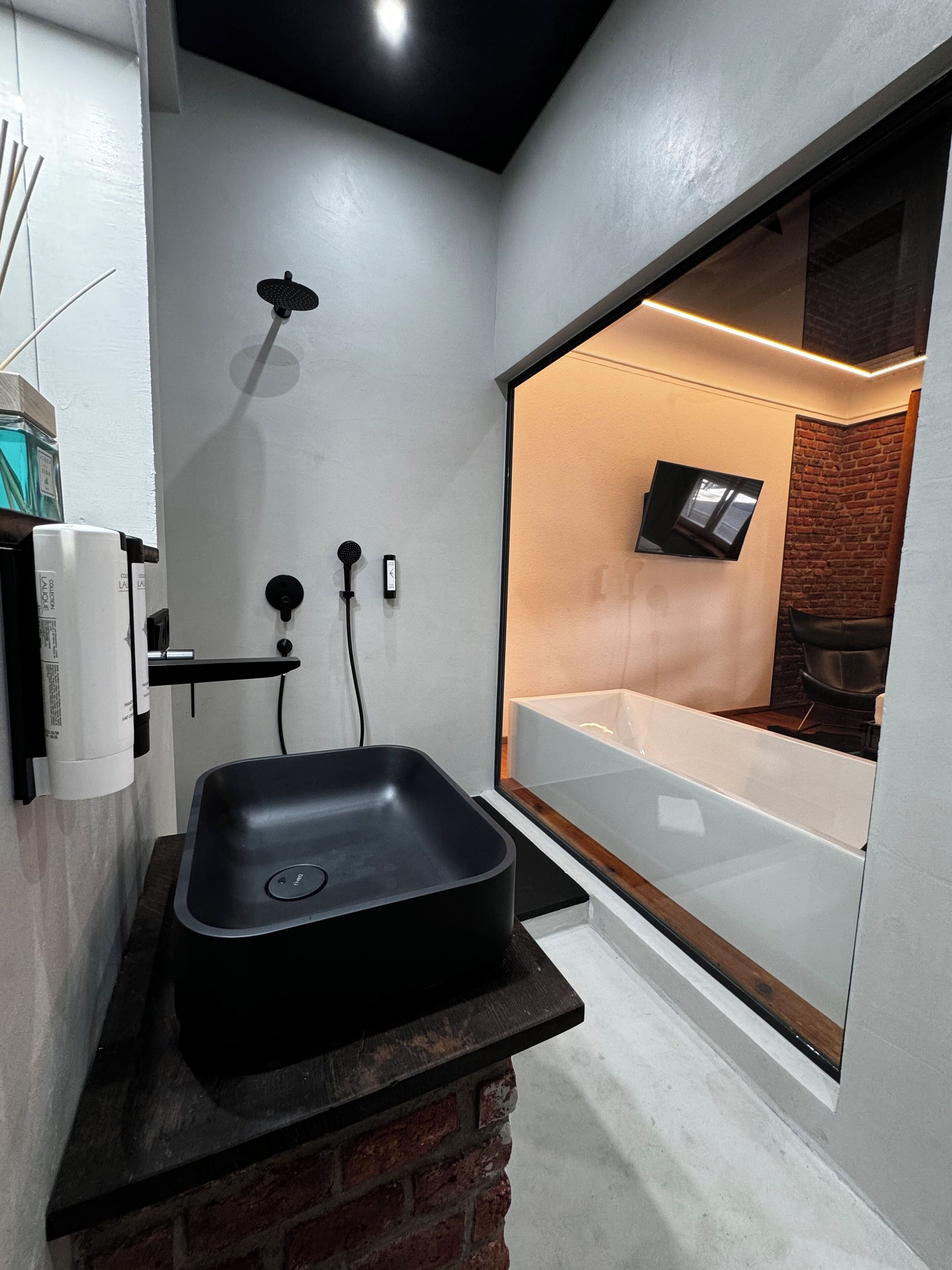 Un baño moderno con un lavamanos negro, un cabezal de ducha de mano y una bañera empotrada.