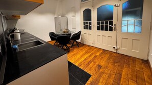 A compact kitchen with a black countertop, a dining table with four chairs, and a wooden floor.