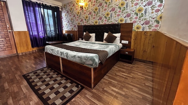 A bedroom with a wooden bed, a nightstand, a wall-mounted lamp, and a floral wallpaper. - Hotel Honey N Spice (Dharamshala)