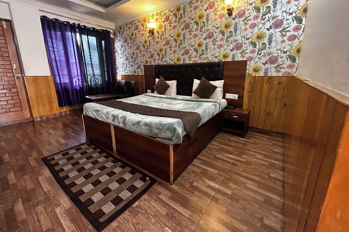 A bedroom with a wooden bed, a nightstand, a wall-mounted lamp, and a floral wallpaper.