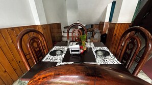 A dining area with a long table set for four, surrounded by wooden chairs. - Hotel Honey N Spice (Dharamshala)