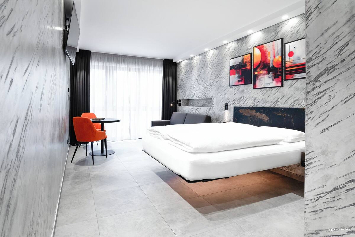 A modern hotel room with a large bed, a desk with a chair, and artwork on the walls.