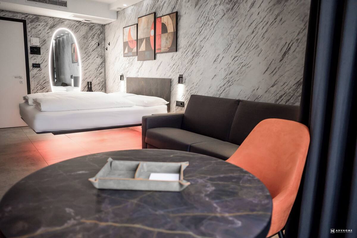 A modern hotel room with a bed, a sofa, a round table, and a large mirror.