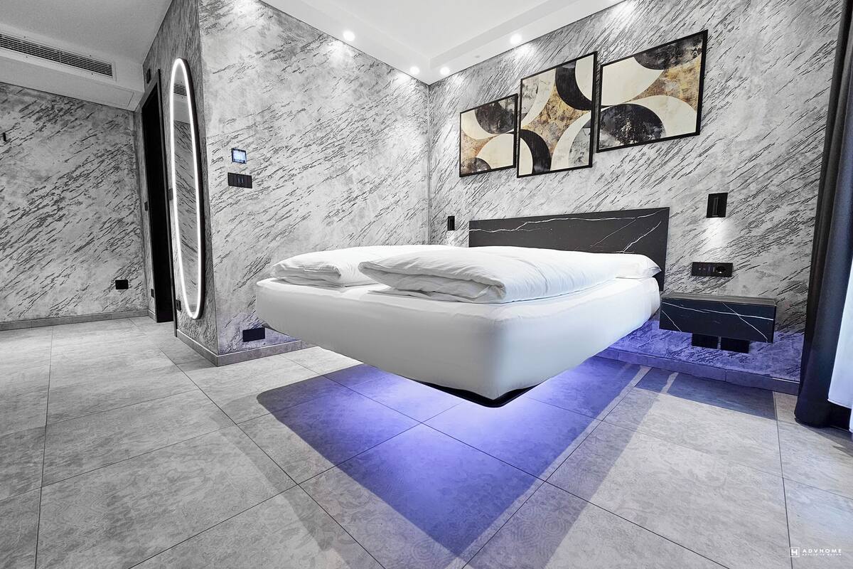 A modern bedroom with a floating bed, marble walls, and abstract artwork.