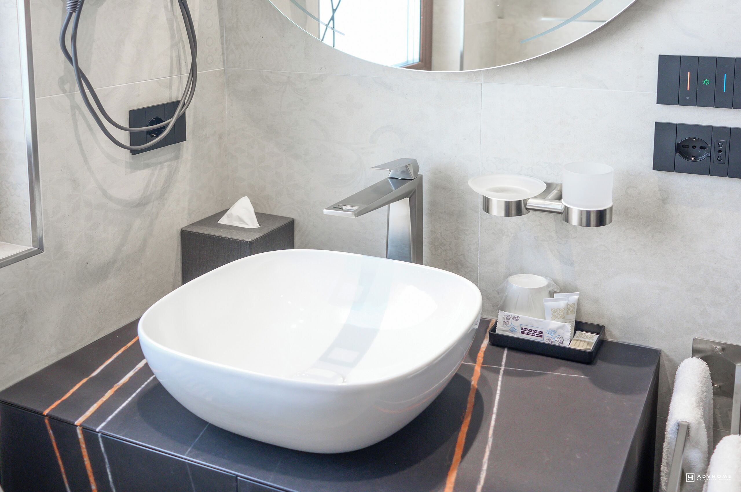 A modern bathroom with a large white vessel sink, a handheld showerhead, a towel rack, and a soap dispenser on the counter.