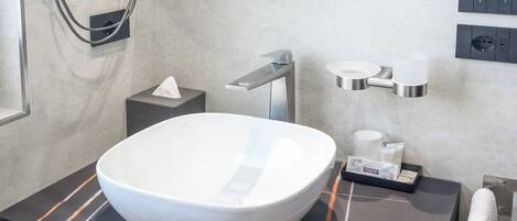 A modern bathroom with a large white vessel sink, a handheld showerhead, a towel rack, and a soap dispenser on the counter.