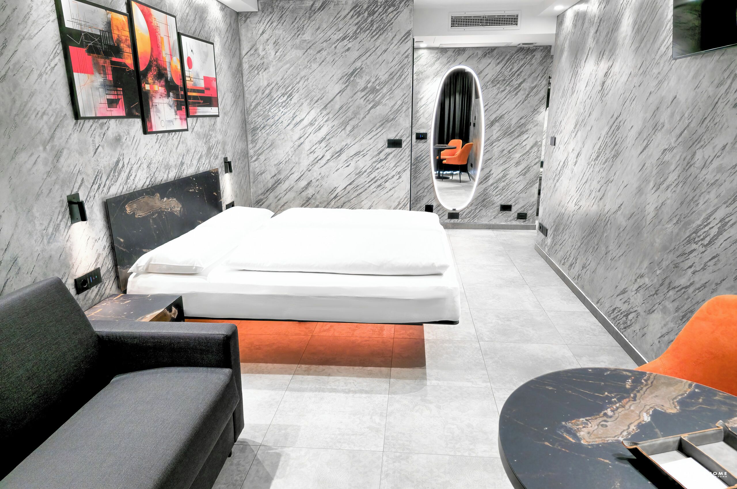 A modern hotel room with a bed, a sofa, a small table, and a mirror.