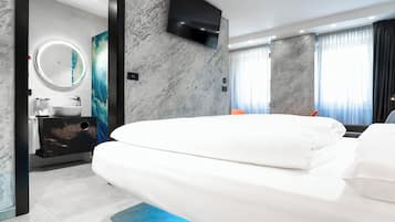 Ein modernes Hotelzimmer mit einem großen Bett, einem runden Spiegel, einem an der Wand montierten Fernseher sowie einem Badezimmer mit Marmorwaschbecken und Waschtisch.