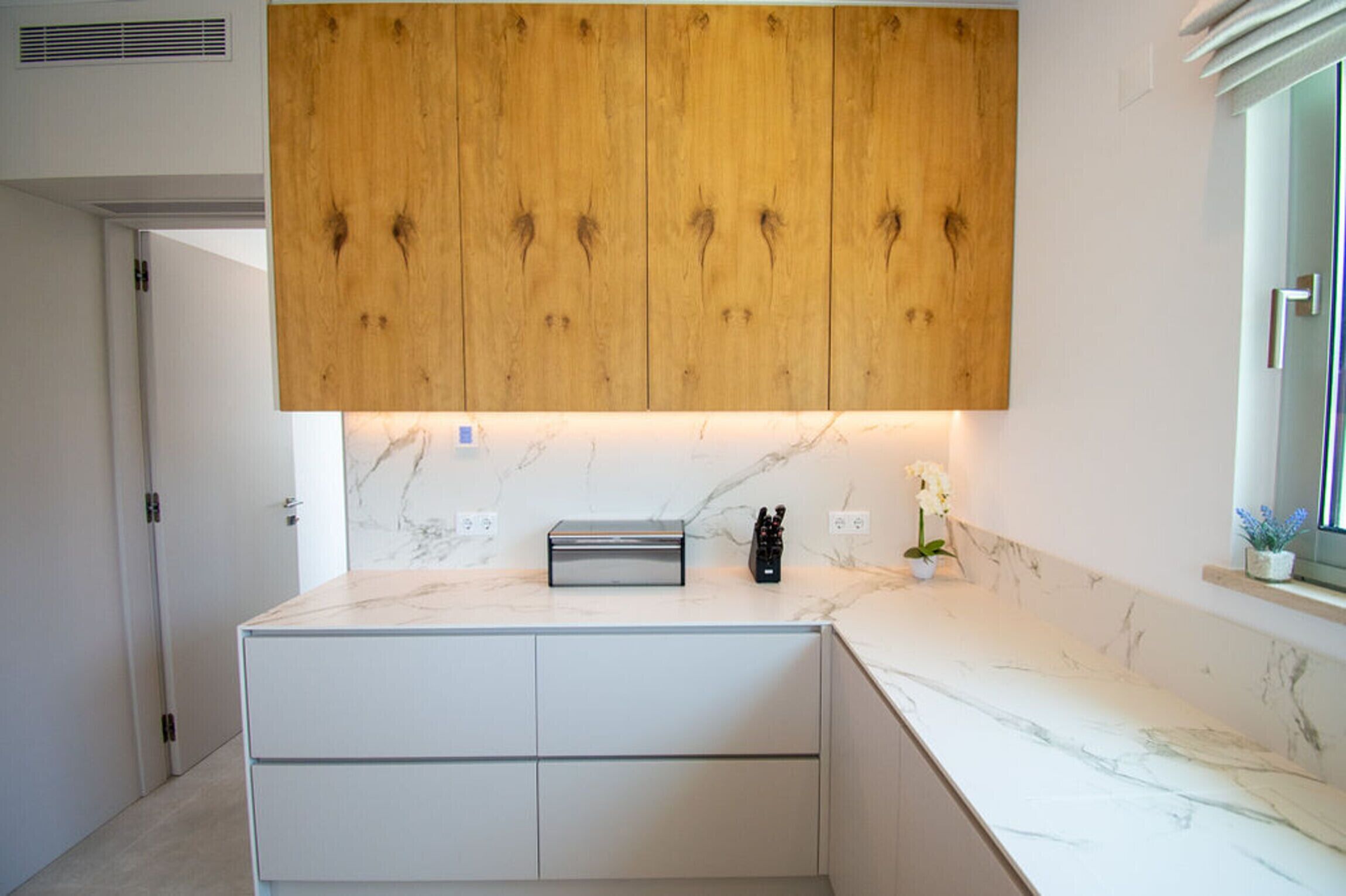 A modern kitchen with wooden cabinets, a marble countertop, and a built-in oven.