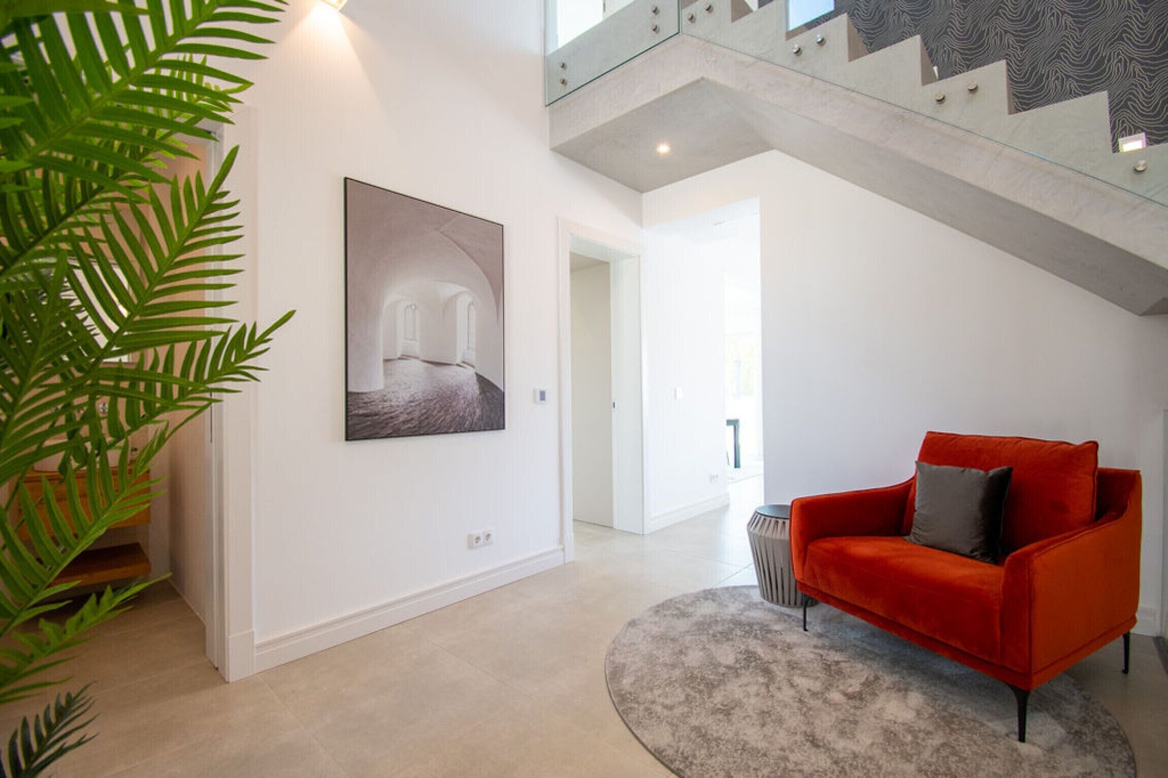 A modern interior with a staircase, a red sofa, and a framed artwork.