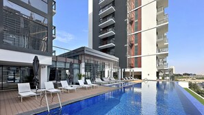Een modern hotel met een zwembad zonder rand aan het dak, ligbedden en een barruimte met glazen wanden.