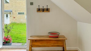Une pièce avec un banc en bois, une petite table et une vue sur un jardin, visible à travers une porte.