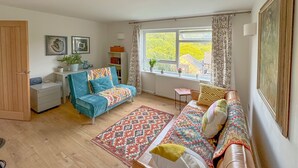 Un salon chaleureux avec un canapé bleu, un tapis à motifs et une vue sur la verdure à l’extérieur.