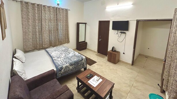 A hotel room with a bed, a sofa, a TV, a ceiling fan, and a small table with a remote control. - Krishnam Guest House (Gwalior)