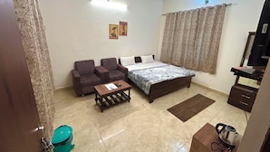 A bedroom with a bed, two sofas, a coffee table, a television, and a ceiling fan. - Krishnam Guest House (Gwalior)