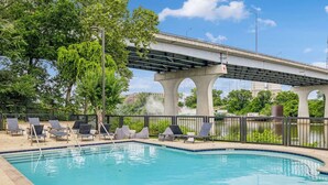 A swimming pool with lounge chairs and a bridge in the background. - Renovated Chic, Riverfront Condo w/ Pool (Nashville)