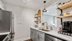 A modern kitchen with stainless steel appliances, wooden shelves, and a marble countertop. - Renovated Chic, Riverfront Condo w/ Pool (Nashville)