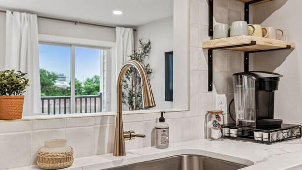 A modern kitchen with a stainless steel sink, a gold faucet, and a coffee maker on a black stand. - Renovated Chic, Riverfront Condo w/ Pool (Nashville)