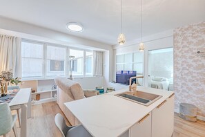 Un appartement moderne et bien éclairé, doté d’une cuisine, d’un coin repas et d’une grande fenêtre laissant entrer la lumière naturelle.